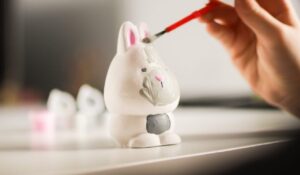 Une personne peint une petite figurine avec un pinceau fin sur un bureau bien éclairé.