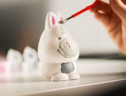 Une personne peint une petite figurine avec un pinceau fin sur un bureau bien éclairé.