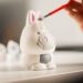 Une personne peint une petite figurine avec un pinceau fin sur un bureau bien éclairé.